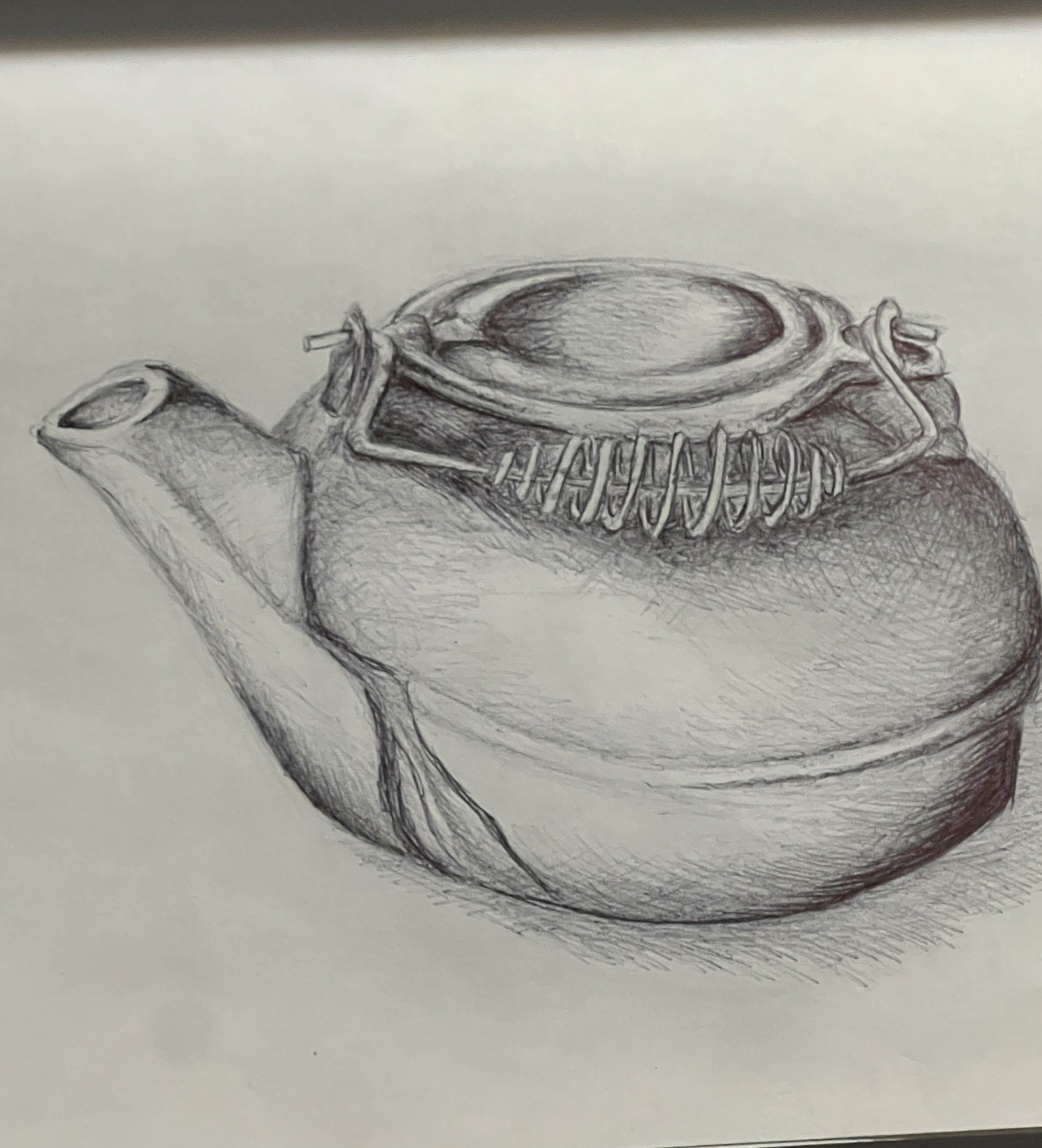 A ballpoint-pen sketch in a spiral-bound sketchbook depicting a traditional cast-iron tea kettle with a curved handle and spout, rendered in detailed cross-hatching to convey its textured surface.
